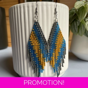 A pair of handmade beaded fringe earrings. Colors in a gradient Grey, Frosted Blue, and Mustard