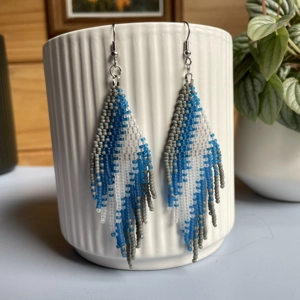A pair of handmade beaded fringe earrings. Colors in a gradient grey, frosted blue, and frosted white
