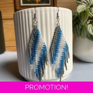 A pair of handmade beaded fringe earrings. Colors in a gradient grey, frosted blue, and frosted white