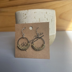 handmade bead-wrapped hoop earrings featuring small seed beads intricately woven around a metal hoop, creating a textured, lightweight design in soft neutral tones, displayed on a branded card. - earthy tones