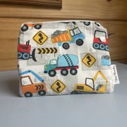 A square, zippered fabric pouch featuring a busy construction vehicle pattern against a light grey, subtly patterned background. The print includes illustrations of colorful work vehicles like a blue cement mixer, a yellow dump truck, an orange excavator, and a red bulldozer, intermixed with yellow diamond-shaped winding road signs. The pouch has a white side tag with 