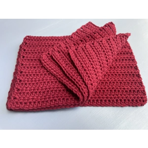A handmade crocheted dishcloth made from red cotton yarn, featuring a textured stitch pattern and soft, neutral tones. The dishcloth is laid flat on a wooden surface.