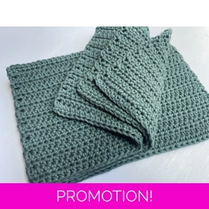 A handmade crocheted dishcloth made from forest green cotton yarn, featuring a textured stitch pattern and soft, neutral tones. The dishcloth is laid flat on a wooden surface.