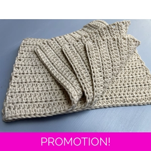 A handmade crocheted dishcloth made from beige cotton yarn, featuring a textured stitch pattern and soft, neutral tones. The dishcloth is laid flat on a wooden surface.