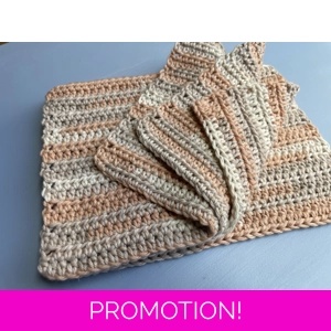 A handmade crocheted dishcloth made from multi hue light orange, and shades of beige cotton yarn, featuring a textured stitch pattern and soft, neutral tones. The dishcloth is laid flat on a wooden surface.