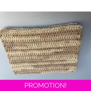 A handmade crocheted dishcloth made from shades of beige cotton yarn, featuring a textured stitch pattern and soft, neutral tones. The dishcloth is laid flat on a wooden surface.