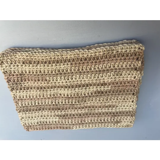 A handmade crocheted dishcloth made from shades of beige cotton yarn, featuring a textured stitch pattern and soft, neutral tones. The dishcloth is laid flat on a wooden surface.