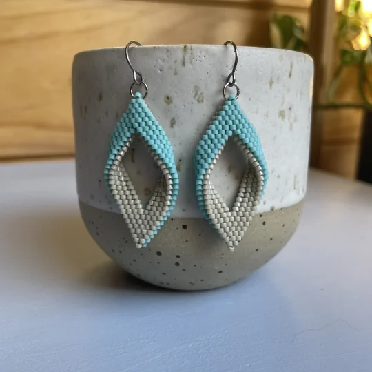 Matte Aqua and beige
 handwoven earrings feature a unique twisted marquise shape, combining clean lines with a gentle three-dimensional curve. Their open design adds a sense of lightness and movement, making them a subtle statement piece for any outfit. Crafted with precision using high-quality Miyuki Delica beads, they’re lightweight, comfortable to wear, and perfect for everyday style or special occasions.