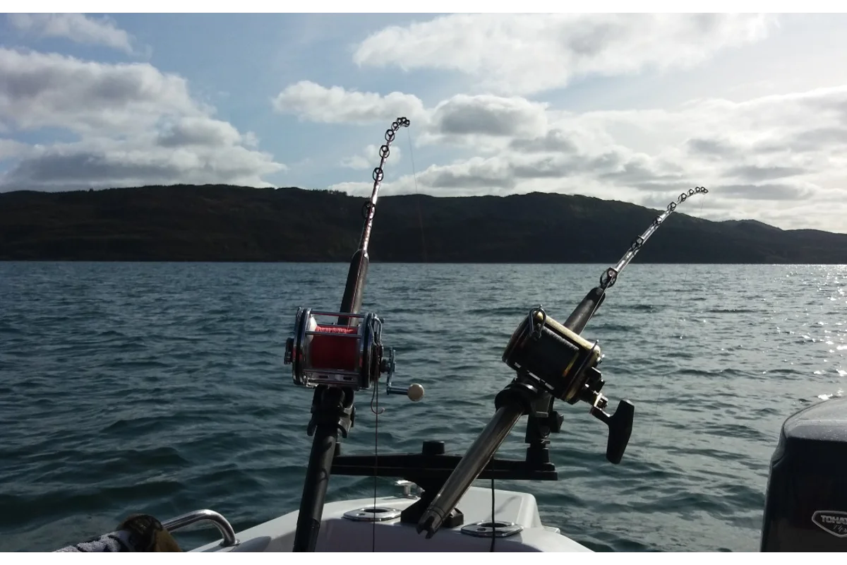 Two sea reels in rod holders on a boat, with a loch and hills behind
